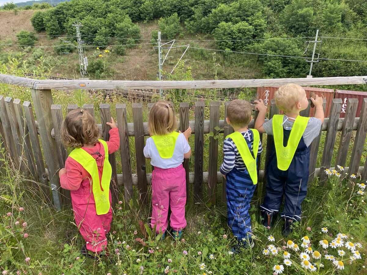 Kinder beobachten vorbeifahrenden Zug hinter dem Holzzaun